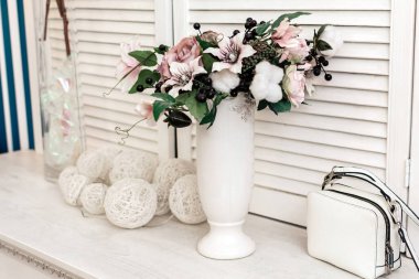 Bir vazo çiçeğin kompozisyonu ve beyaz ahşap bir masada bir kadın çantası.