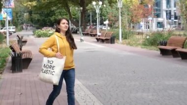 Turuncu kapüşonlu esmer bir kadın elinde kumaş bir çantayla şehirde daha fazla plastiğe yer yok diyor.