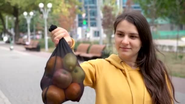 Seorang wanita berambut cokelat menunjukkan kantong kain jala buah dengan sayuran dan buah-buahan. — Stok Video