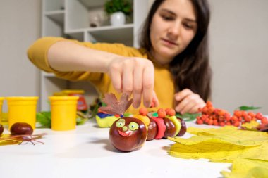 Bir kadın viburnum çileğiyle dekore eder kestane ve plastikten yapılmış bir sonbahar sanatı tırtılı