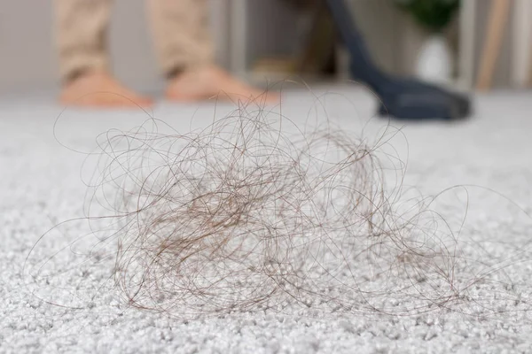 A clump of long hair on the carpet and a vacuum cleaner close-up