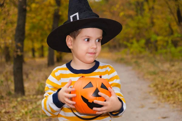 Un niño de preescolar sostiene una calabaza con dulces en el bosque de Halloween de otoño. —  Fotos de Stock