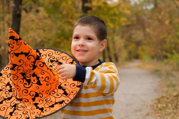 Un niño con una chaqueta a rayas sostiene un gran sombrero naranja con murciélagos. —  Fotos de Stock