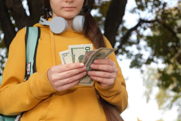 Dospívající dívka ve sluchátkách počítá dolarové bankovky, kapesné — Stock fotografie
