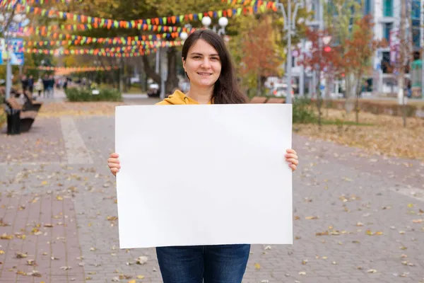 25 yaşında esmer bir kadın gülümsüyor ve elinde yazı ve yazı için boş beyaz bir çarşaf tutuyor.