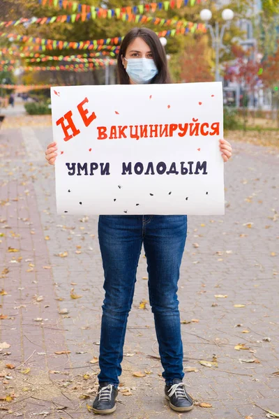 Žena v ochranné masce drží plakát, který říká rusky, překlad: Nenechte se očkovat zemřít mladý. — Stock fotografie