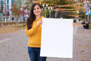 Esmer bir kadın gülümser ve yazı ve yazı için boş beyaz bir çarşaf tutar.