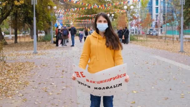 Een vrouw heft een poster op met Russische tekst, vertaling uit het Russisch: Vaccineer niet jong. — Stockvideo