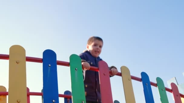 Küçük bir çocuk gökyüzüne karşı oyun parkındaki bir çocuk şatosunun köprüsüne atlıyor.. — Stok video