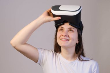 Sanal gerçeklik gözlüklü bir kadın gri bir arka plana bakıyor..