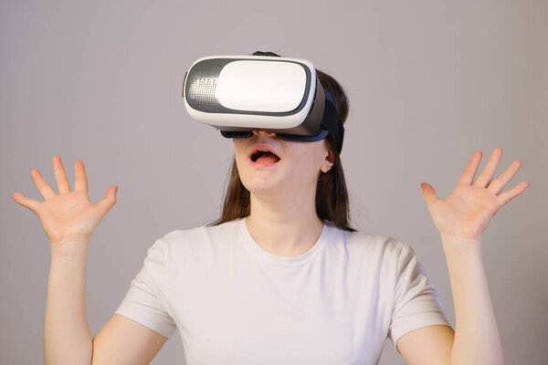 A woman in virtual reality glasses with her mouth open raises her hands