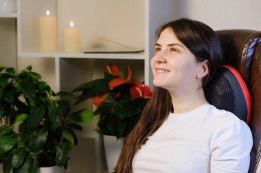 Bir kadın masaj yastığıyla bir sandalyeye oturur ve boyun masajı yapar..