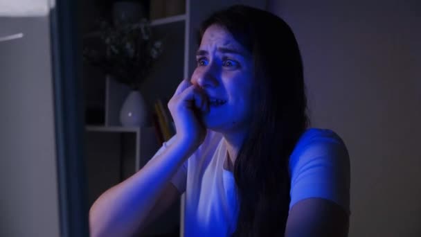 Uma mulher assiste a um filme de terror no escuro, mordendo as unhas da experiência — Vídeo de Stock