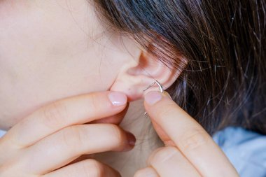 Bir kadın kulağına altın bir küpe takıyor..