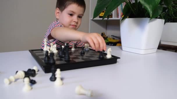 Мальчик 4 лет играет в шахматы, балует и катает тур по столу — стоковое видео