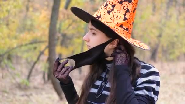 Een vrouw in een heksenkostuum draagt een beschermend medisch masker in het bos. — Stockvideo