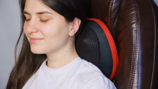 Uma mulher senta-se em uma cadeira com um travesseiro de massagem e faz uma massagem no pescoço. — Vídeo de Stock