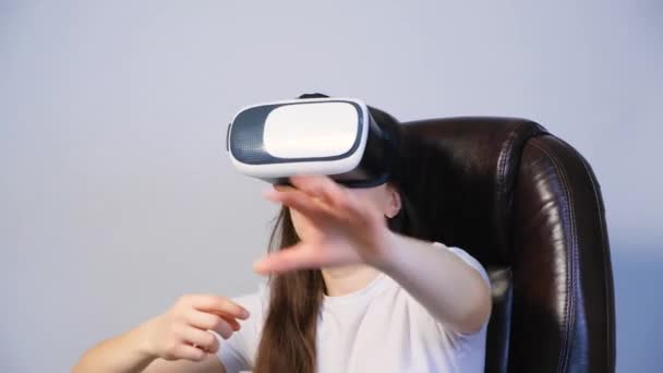 O femeie cu ochelari de realitate vitruală stă într-un scaun și își mișcă mâinile. — Videoclip de stoc