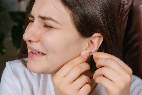 A woman tries to put an earring in her ear, earlobe problem, the hole is overgrown — Stock Photo, Image