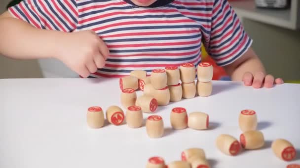 Een kind in een gestreept T-shirt speelt met houten bingovaten, bouwt en vernietigt torens — Stockvideo