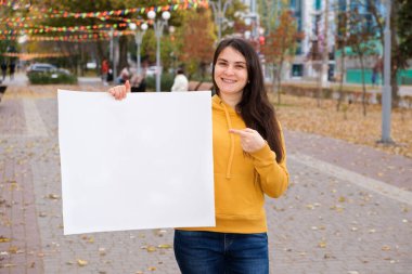 Genç beyaz bir kadın parmağını boş bir kağıda doğrultup gülümsüyor.
