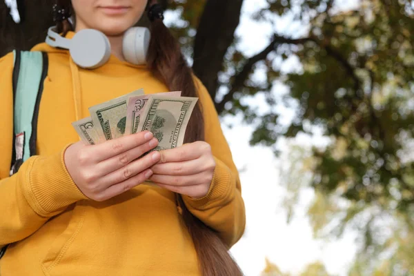 Дівчинка-підліток в навушниках рахує доларові купюри, кишенькові гроші — стокове фото