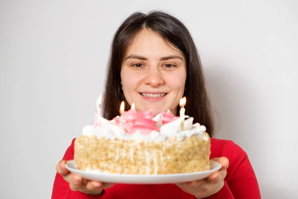 赤い服のブルネットの女性はキャンドル付きの大きな白いケーキを保持し 願いを作ります — ストック写真