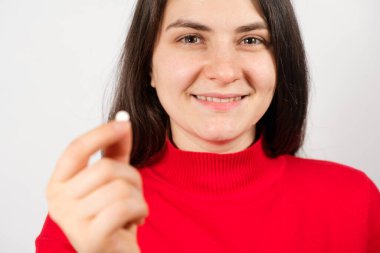 Bir kadın beyaz arka planda elinde bir hap tutuyor. Hastalıkların tedavisi, beslenme takviyeleri ve farmakoloji