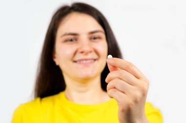 Bir kadın beyaz arka planda elinde bir hap tutuyor. Hastalıkların tedavisi, beslenme takviyeleri ve farmakoloji