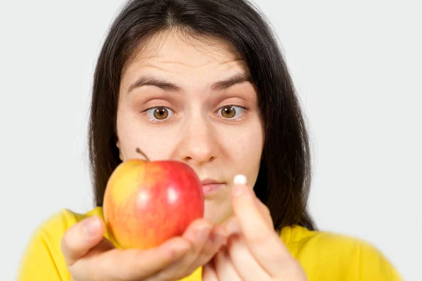 A woman in yellow holds an apple and a pill in her hands. Vitamins in natural form and in synthetic, dietary supplements Stock Image