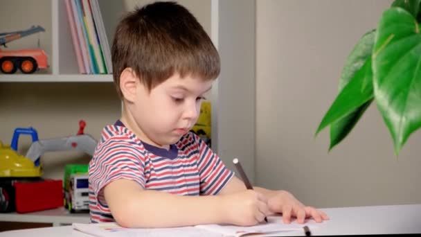 Uma criança de 4 anos aprende a escrever um livro, senta-se corretamente à mesa, mantém as costas retas. — Vídeo de Stock