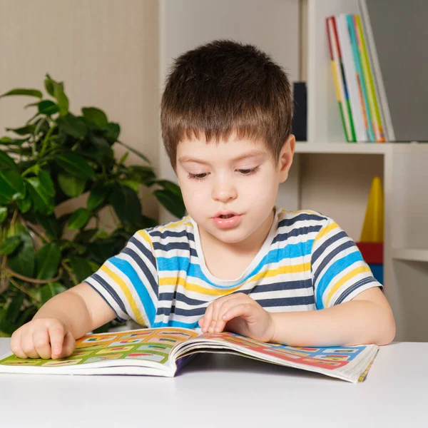 4-річна дитина сидить за столом і читає книгу, дивиться на картинки, вчиться читати . — стокове фото