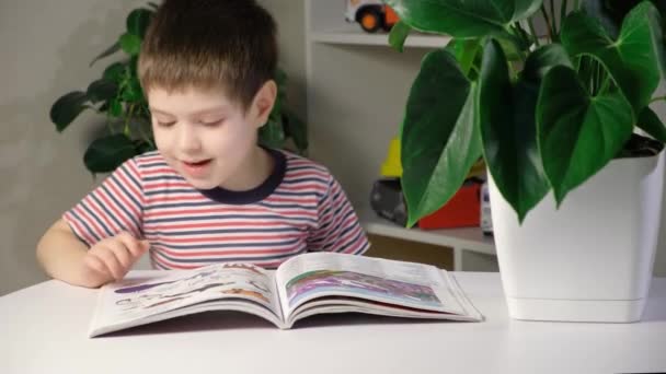 Un garçon heureux de 4 ans regarde un livre avec des photos, montre des photos et les nomme — Video