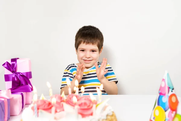 Un guapo niño preescolar con un pastel en su cumpleaños aplaude sus manos sobre un fondo blanco. — Foto de Stock