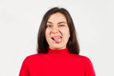 Kırmızı kazaklı, dilinde beyaz bir hapla ağzı açık bir kadın huysuz bir şekilde kıvranıyor.