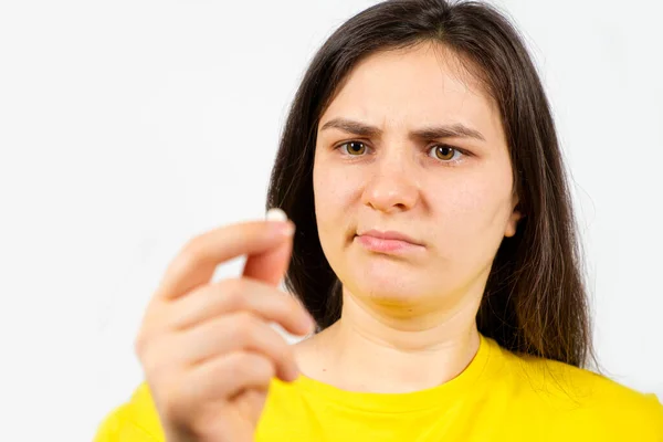 Una mujer con la cara descontenta tiene una pastilla en la mano. Daño por el tratamiento con medicamentos, desconfianza en la farmacología —  Fotos de Stock