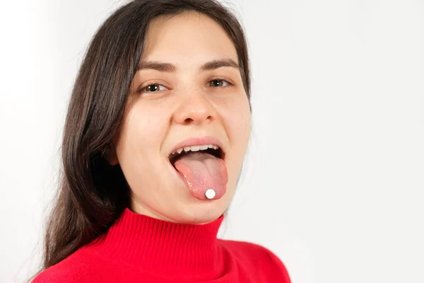 Eine gesunde junge Frau in Rot mit Pillen auf der Zunge lächelt und blickt vor weißem Hintergrund in die Kamera — Stockfoto