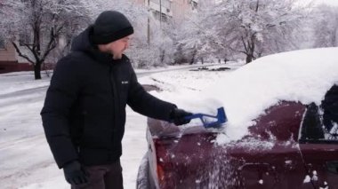 Bir adam kardan arabayı temizler, kışın karları yüzeyden temizler.