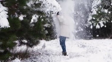 Çam ormanında beyaz ceketli bir kadın kar altında kar altında kar altında atlıyor ve eğleniyor.