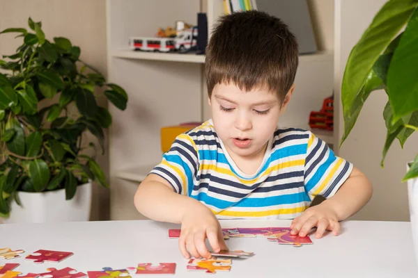 Un bambino in età prescolare gioca puzzle, mette insieme un quadro — Foto Stock