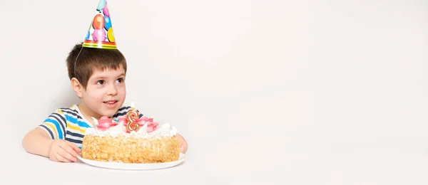 A boy celebrates his third birthday sitting at a table on a white background with a cake, looking away. — Stock Photo, Image