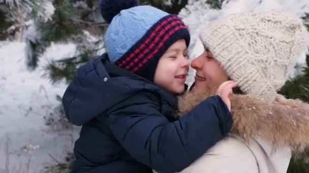 Moeder en zoon wrijven hun neus in, bewonderen elkaar op straat in de winter in een besneeuwd bos, vreugde en geluk in het skigebied. — Stockvideo