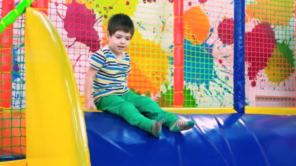 Een vrolijke jongen glijdt van de glijbaan in zachte multi-gekleurde kubussen in een kinderspeelplaats. — Stockvideo