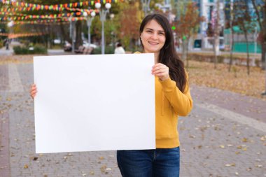 Esmer bir kadın gülümser ve yazı ve yazı için boş beyaz bir çarşaf tutar.
