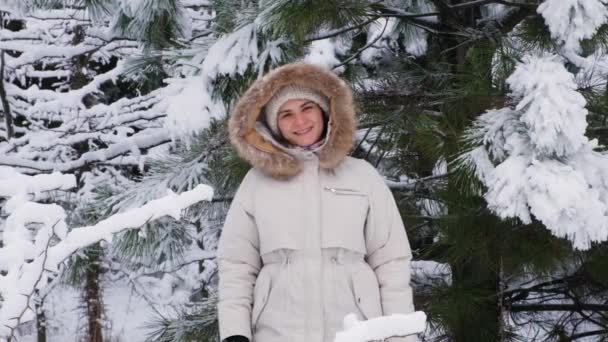 Vrouwelijke video portret slow-motion schieten, een vrouw in een winter besneeuwd bos glimlacht kijken naar de camera, sneeuwvlokken vliegen door. — Stockvideo