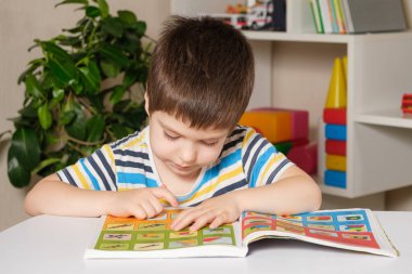 4 yaşındaki bir çocuk masaya oturur, kitap okur, resimlere bakar, okumayı öğrenir..