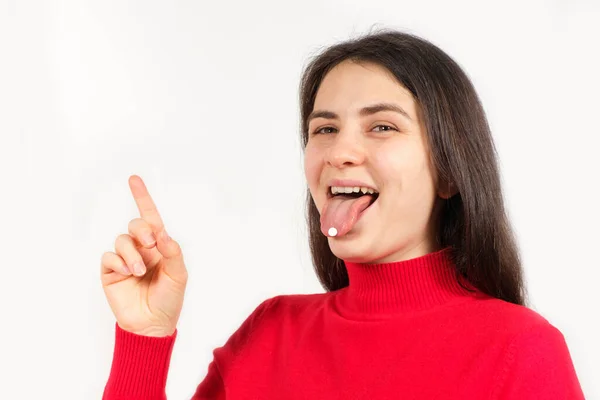 A woman in red with pills on her tongue points her finger at a place for text — Stock Photo, Image