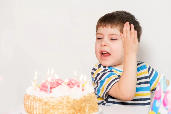 El chico está molesto, celebrando su cumpleaños, llorando sentado en la mesa con un pastel, un lugar para el texto. — Foto de Stock