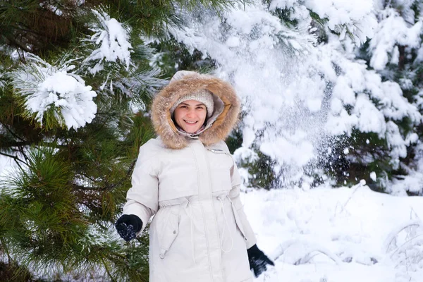 Una donna in una foresta innevata invernale sorride guardando la macchina fotografica, i fiocchi di neve volano. — Foto Stock