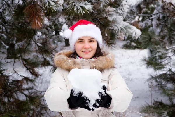 Kobieta w czapce Mikołaja trzyma śnieżną kulę w dłoniach w zimowym lesie pokrytym śniegiem, miejsce na tekst — Zdjęcie stockowe